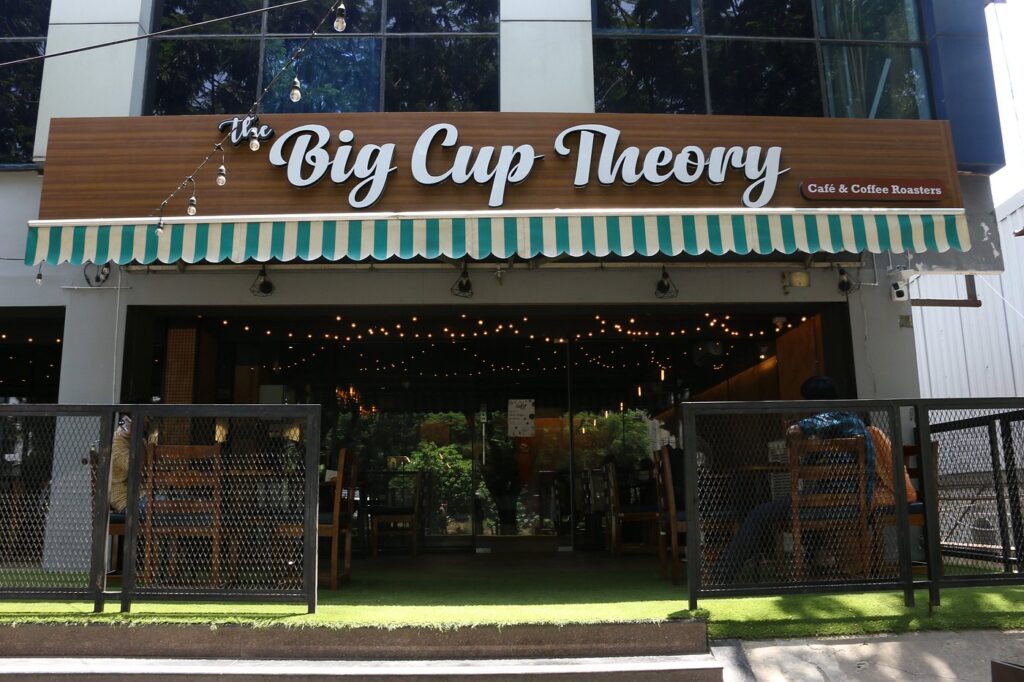 The Big Cup Theory Café entrance showcasing contemporary architecture and a cozy outdoor dining space.